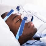 High Angle View Of A Young African Man Wearing CPAP Mask Sleeping On Bed