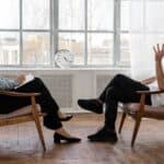 Person in Black Pants and Black Shoes Sitting on Brown Wooden Chair